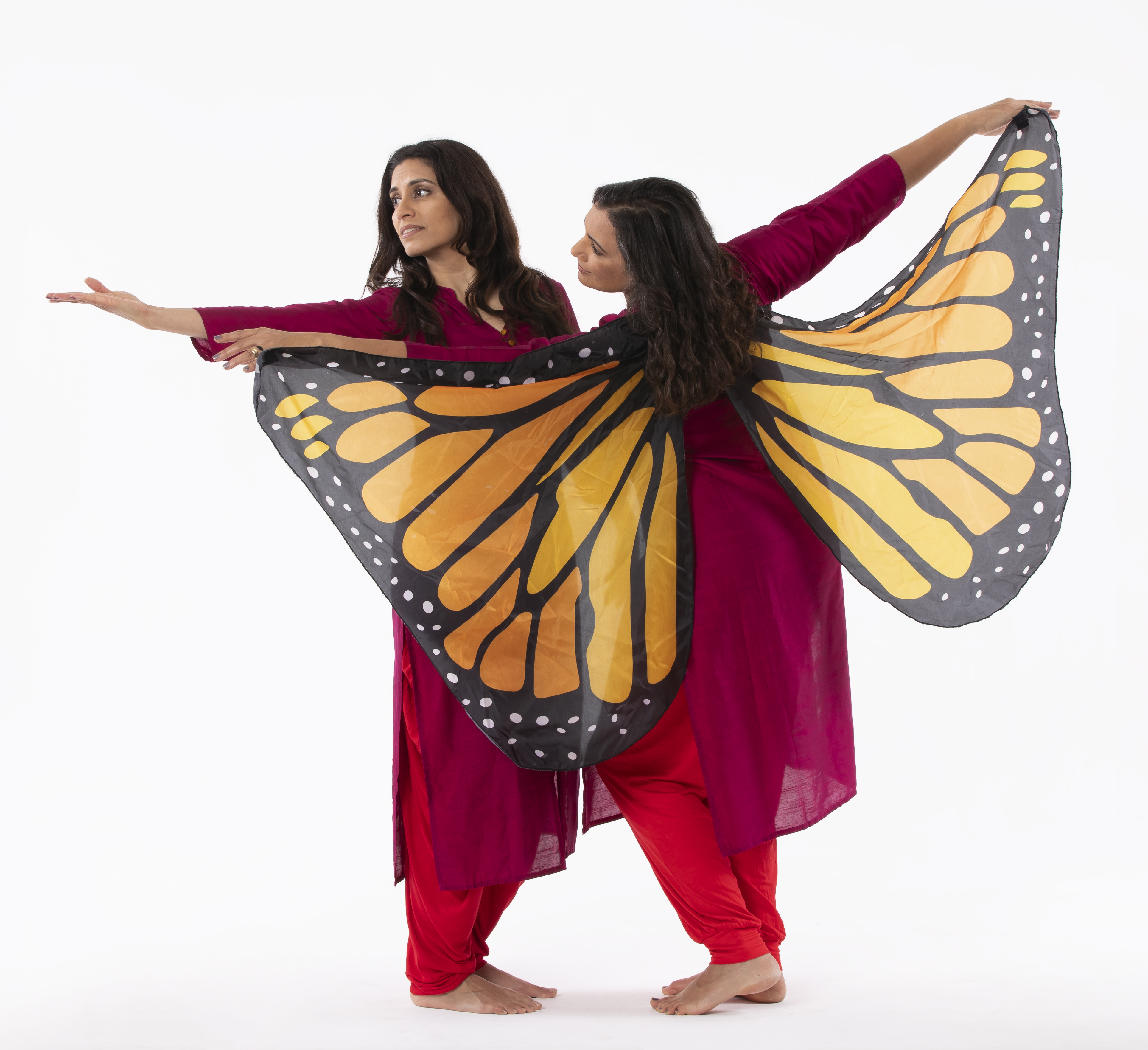 Two dancers in red reaching to the side, one with giant monarch butterfly wings spread wide.