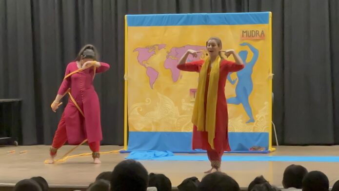 Performing in front of an audience of kids, Danish is wrapped in a rope net with her head down while Tulsi is smiling pointing at her face.